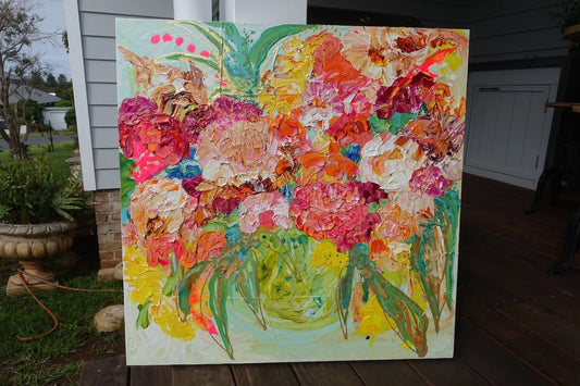 Pink, cream and yellow blooms in a green vase against a pale green background. Inset on a deck.