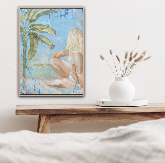 pastel painting of a girl in a bikini sitting under a banana tree. Shown in situ on a white wall above a timber bench and a white vase of dried leaves.