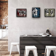 Load image into Gallery viewer, Three black and white cows standing side by side, serenely gazing straight ahead, against a maroon background.  Shown in situ on a grey panelled wall with two other paintings of cows arranged side by side.
