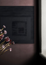 Load image into Gallery viewer, An abstract painting that at first appears totally black but on closer observation  you can notice geometrical shapes within the painting. Shown in situ on a mulberry coloured wall.
