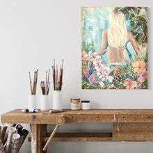 Load image into Gallery viewer, Bikini girl standing amongst tropical flowers against a pastel blue background. In situ on  a wall above a wooden block with paint brushes and tins of paint.
