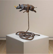 Load image into Gallery viewer, Bronze sculpture of a rhino with a gold horn, suspended on a bronze rope.

