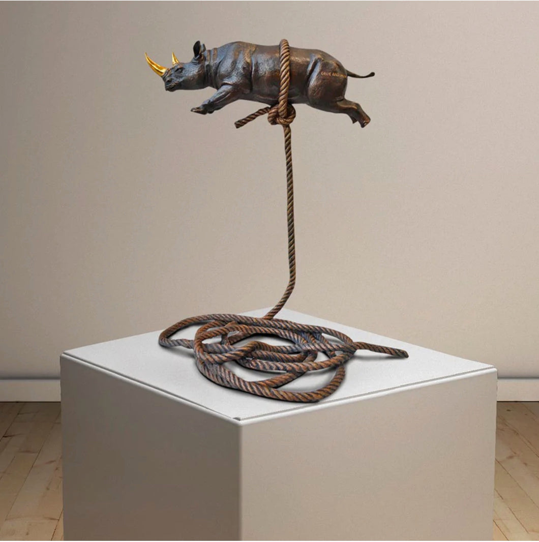 Bronze sculpture of a rhino with a gold horn, suspended on a bronze rope.