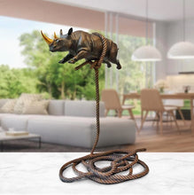Load image into Gallery viewer, Bronze sculpture of a rhino with a gold horn, suspended on a bronze rope. In situ on a marble table.
