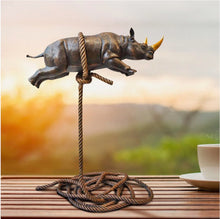 Load image into Gallery viewer, Bronze sculpture of a rhino with a gold horn, suspended on a bronze rope. In situ on a timber table next to a cup and saucer.

