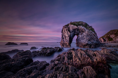 A photographic print of Horse Head Rock at Bermagui, on the NSW South Coast, against a pink and purple sky.