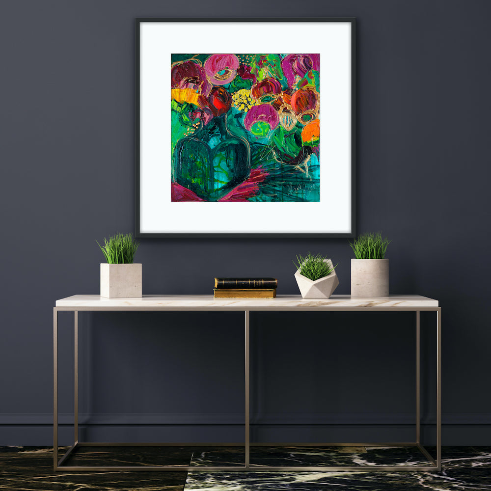 A magnificent bunch of vibrant blooms in a turquoise glass vase against a turquoise, green and magenta background, framed in black on a blue wall.
