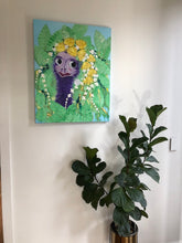 Load image into Gallery viewer, A quirky colourful painting of an emu with flowers in her hair and a dress of leaves. Shown in situ on a white wall.
