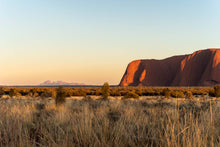 Load image into Gallery viewer, Kata Tjuta glows with sunrise in the distance beyond Uluru.
Uluru, Northern Territory
