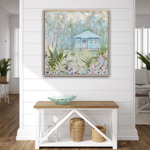 Load image into Gallery viewer, An idyllic pale blue beach cottage with white trim on the windows and verandah. The house is surrounded by palm trees, with a white puppy on the grass in front of the cottage and a garden with fern fronds and flowers. Shown in situ against a white wall.
