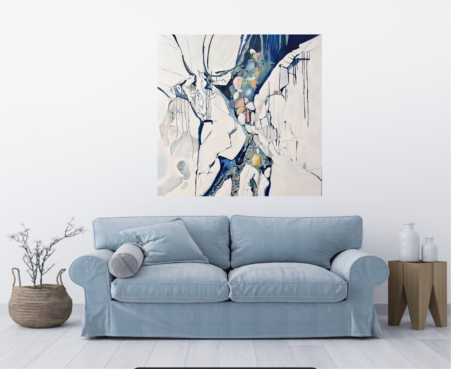 Abstract painting in shades of blue, white, turquoise, pink and yellow. Shown in situ on a white wall above a blue sofa.