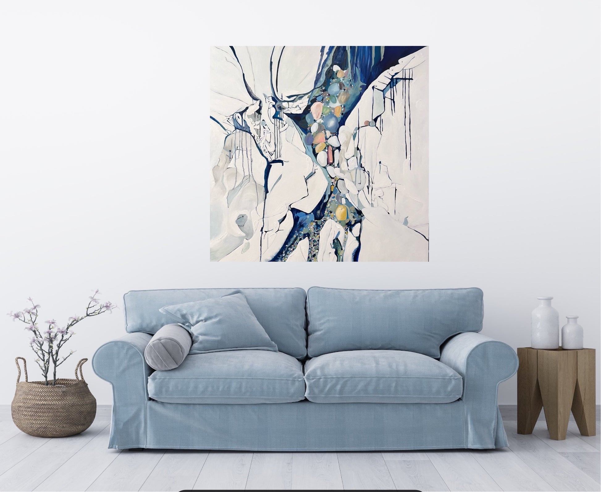 Abstract painting in shades of blue, white, turquoise, pink and yellow. Shown in situ on a white wall above a blue sofa.