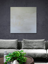 Load image into Gallery viewer, A white on white abstract painting. Within the painting are words and marks. Shown in situ on a charcoal wall above a pale grey sofa.
