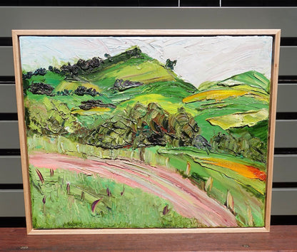 Abstract landscape of rolling green and yellow hills and a winding pink road.  Framed.