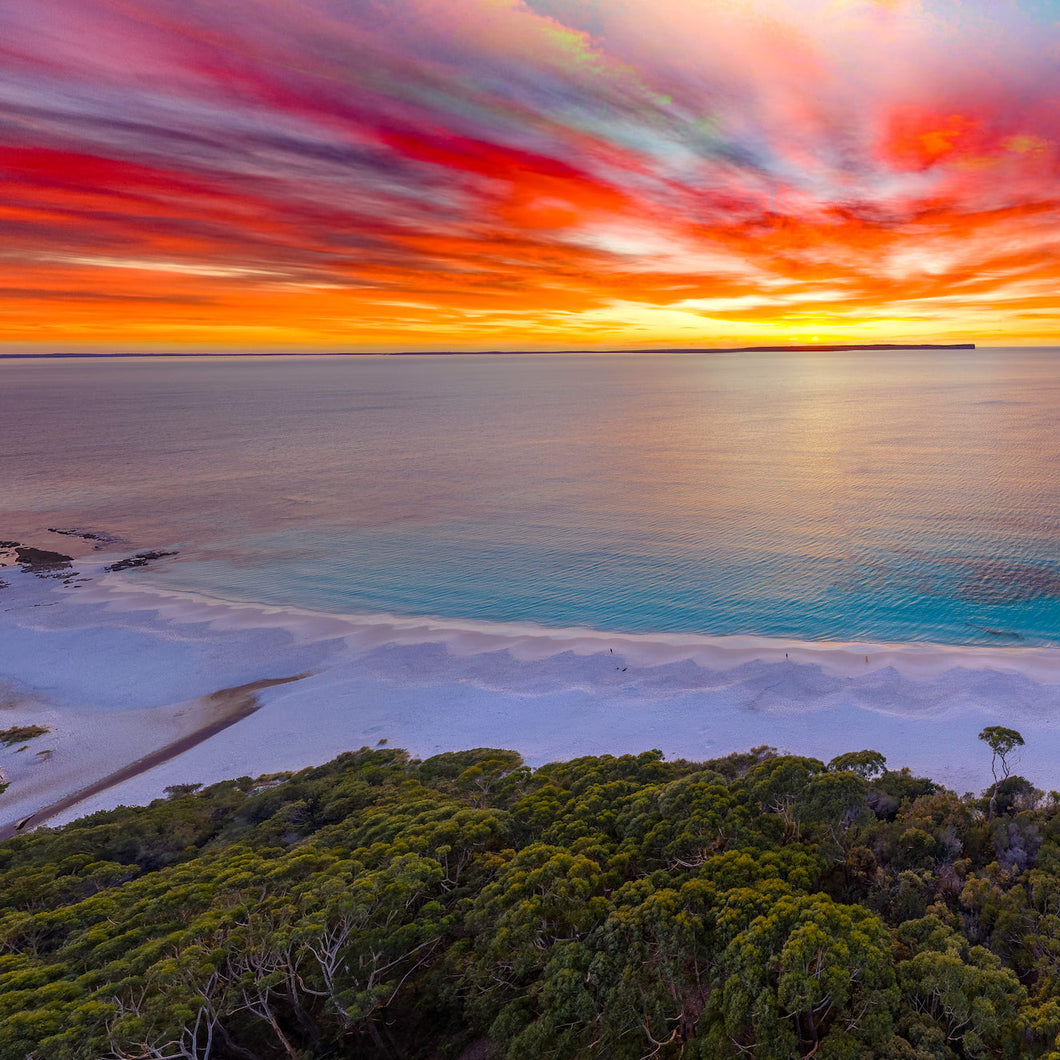 Hyams Beach, Jervis Bay NSW at sunrise with a vibrant orange and yellow sky above the white sand and turquoise waters of the Bay. Square view.