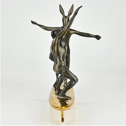 Bronze sculpture of a dog man and rabbit woman on a surfboard with gold patina. Back view.