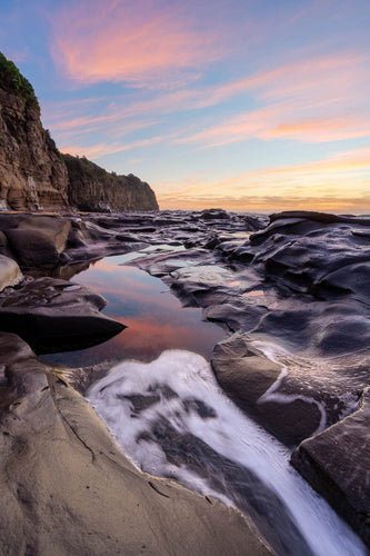 A beautiful sunrise sky reflects in the rock pools of Walkers Beach. Gerringong, Australia