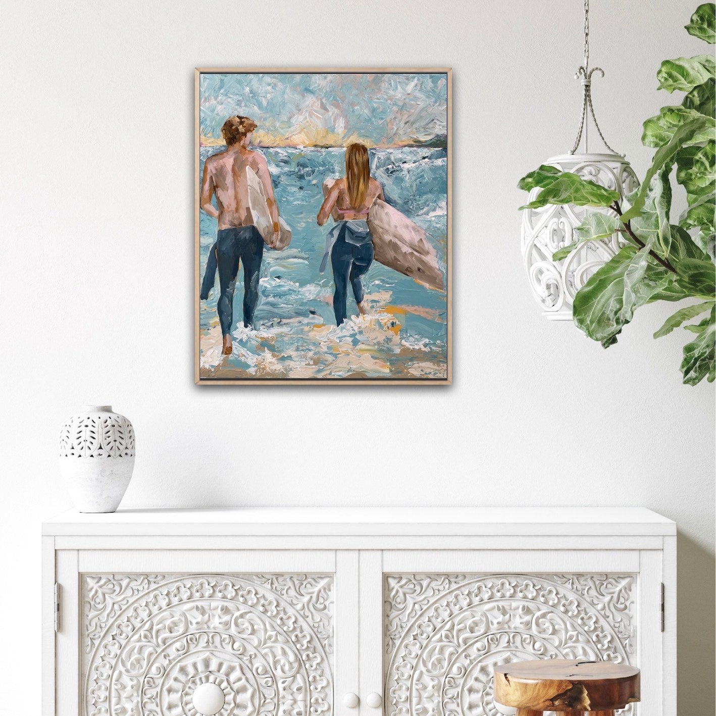 Surf painting with a man and woman standing on the edge of the ocean with surfboards under their arms. Shown on a white wall.